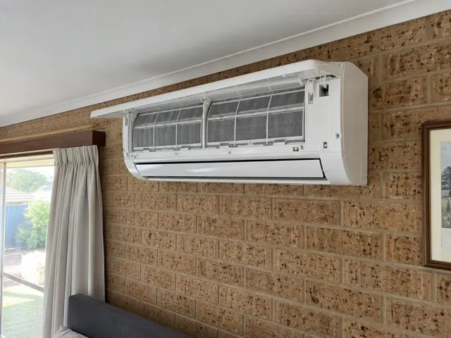 Clean split system indoor head with open front panel and visible filters on a brick wall in Elizabeth North