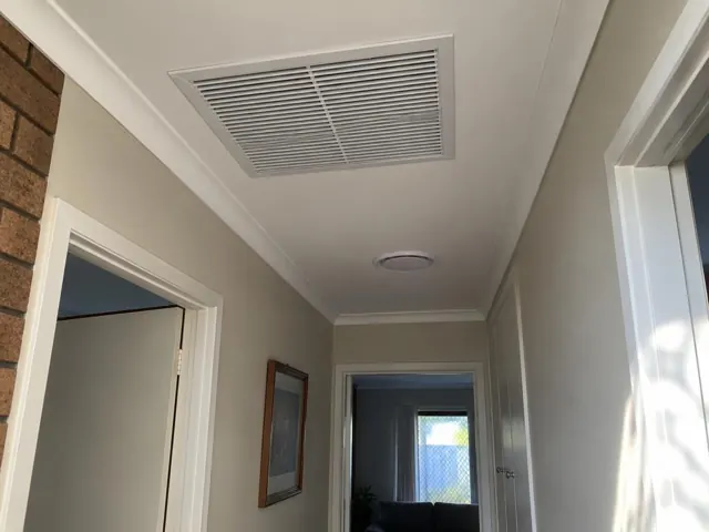 Ceiling return-air grille and round outlet in a hallway with plaster walls in Davoren Park