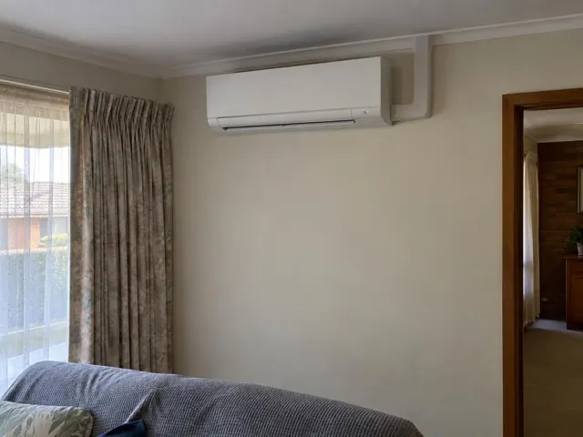Wall-mounted split system above a lounge room sofa beside curtained window and doorway in Elizabeth North